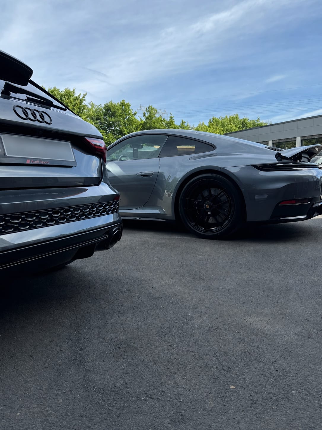 Grauer Audi RS neben einem grauen Porsche 911 im Freien unter blauem Himmel, zwei Premiumfahrzeuge frisch aufbereitet.