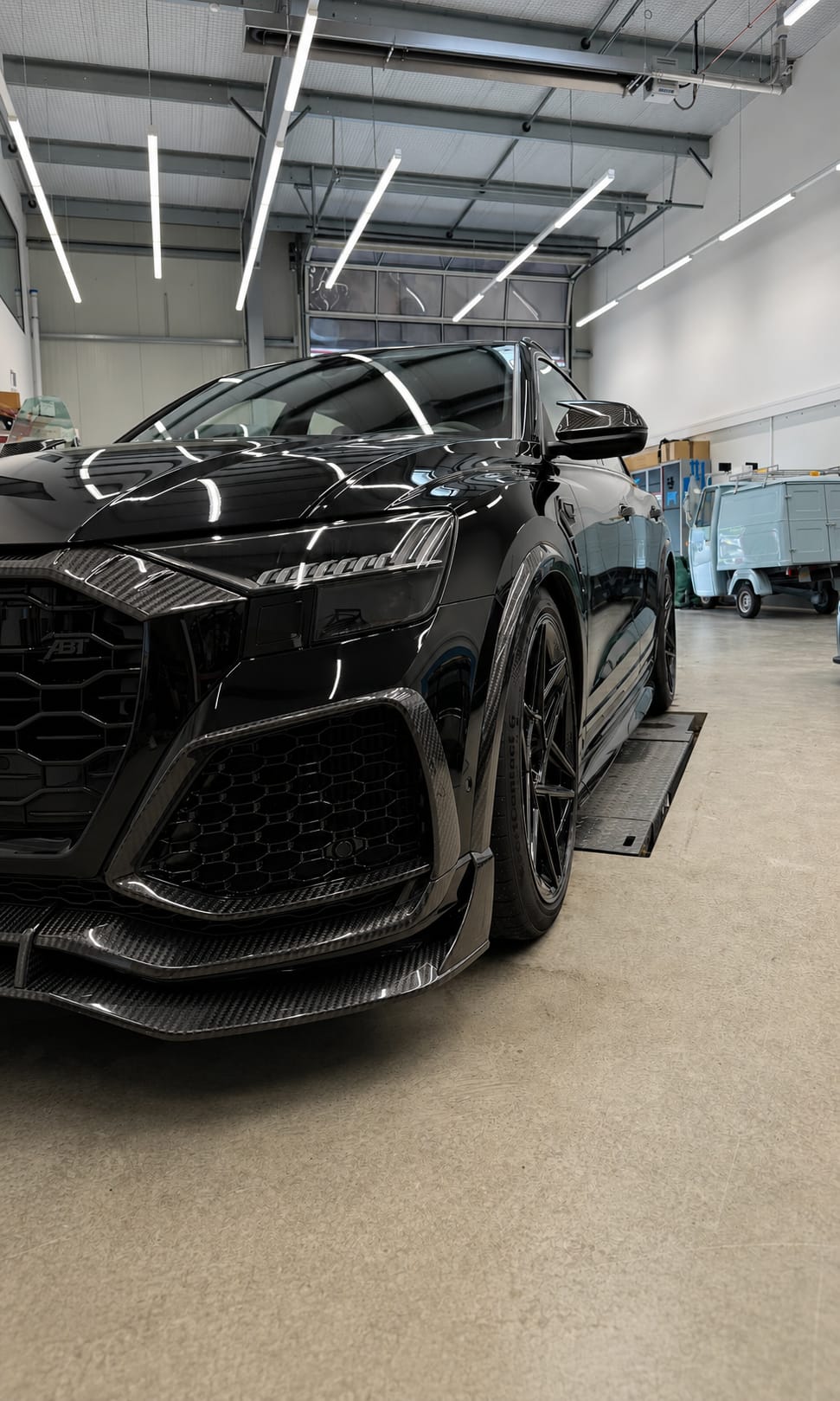 Schwarzer Audi RS Q8 mit Carbon-Anbauteilen frontal in der Aufbereitungshalle, frisch aufbereiteter Lack mit klaren Lichtreflexen.