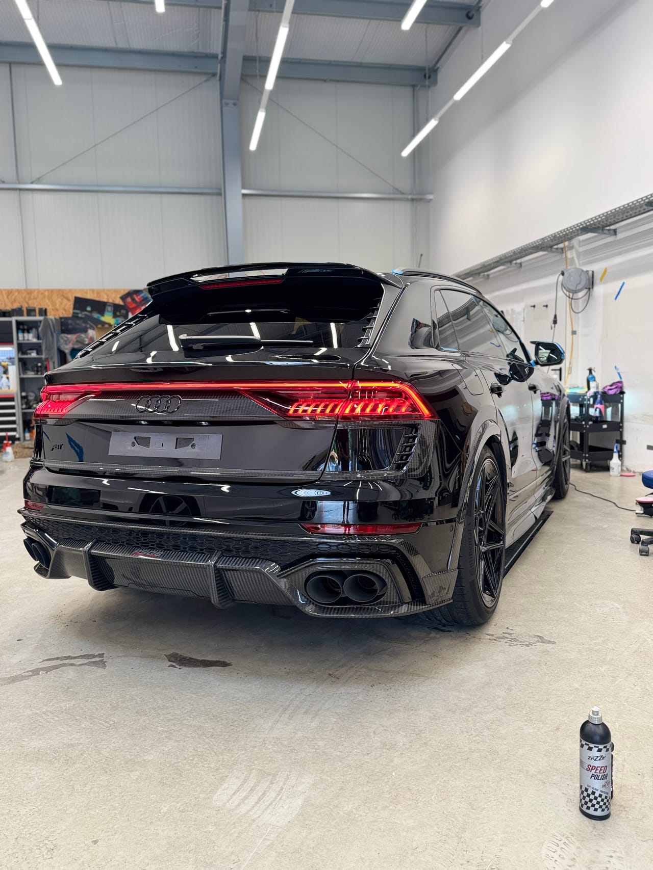 Heckansicht eines schwarzen Audi RSQ8 mit Carbon-Diffusor in der Halle, daneben eine Flasche Politur.