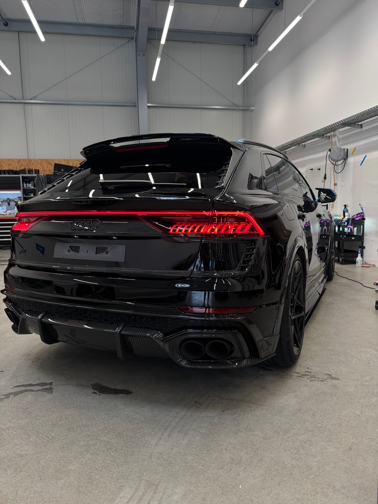 Schwarzer Audi RSQ8 von hinten in der Aufbereitungshalle, Heckleuchten und Carbon-Heck deutlich sichtbar.
