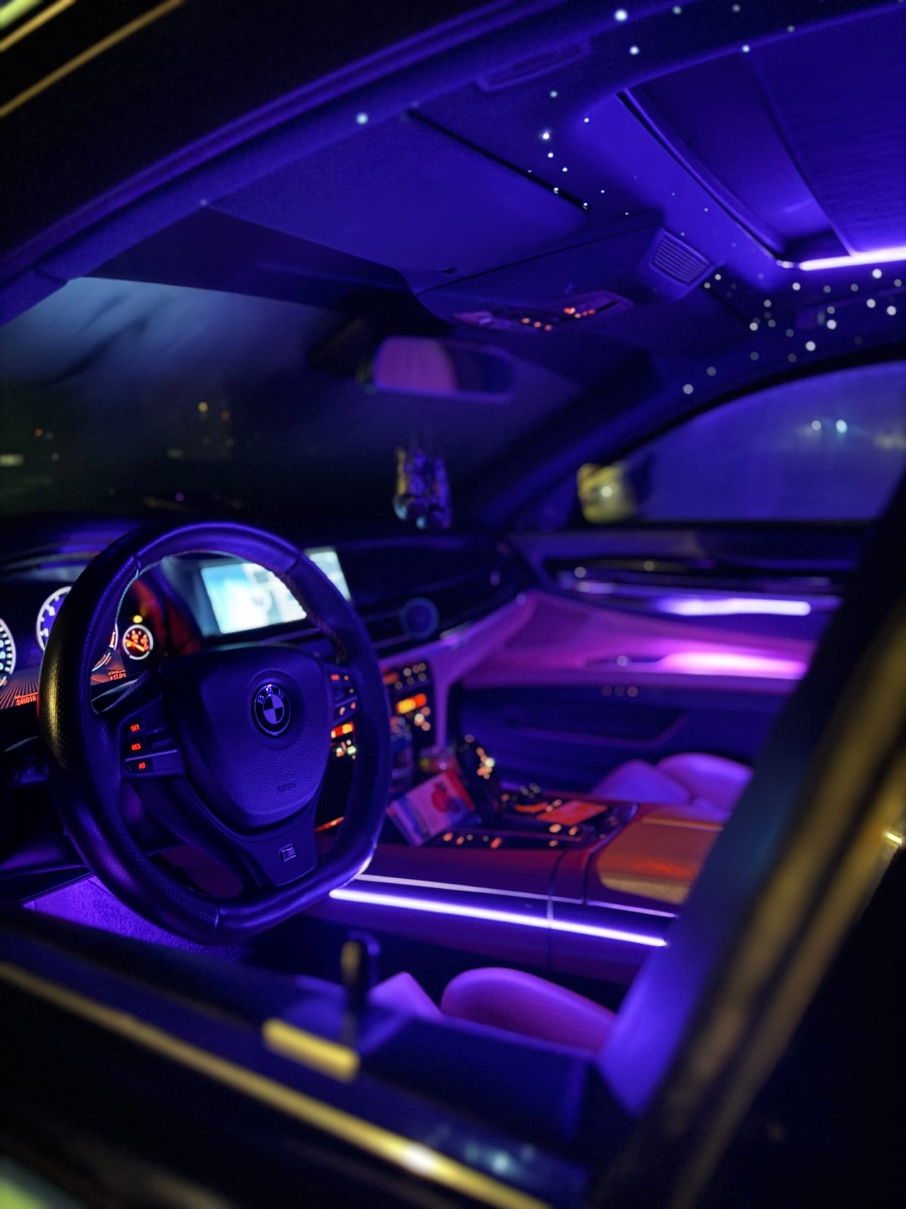 Cockpit eines BMW 7er bei Nacht mit blau-violetter Ambientebeleuchtung und beleuchtetem Lenkrad.