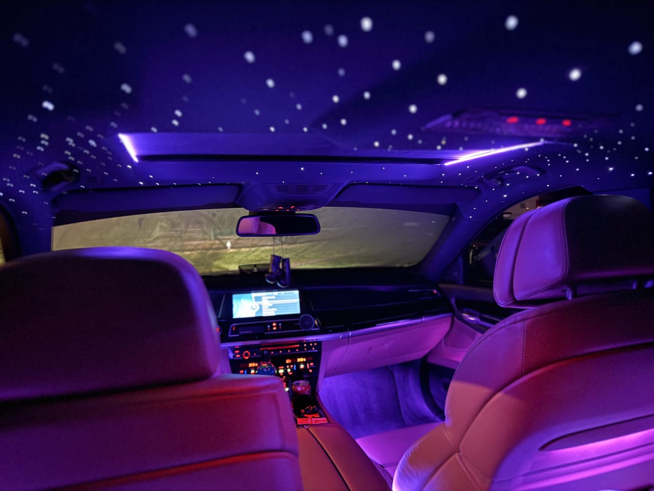 Beleuchteter Sternenhimmel-Dachhimmel über dem vorderen Innenraum eines BMW 7er bei Nacht.
