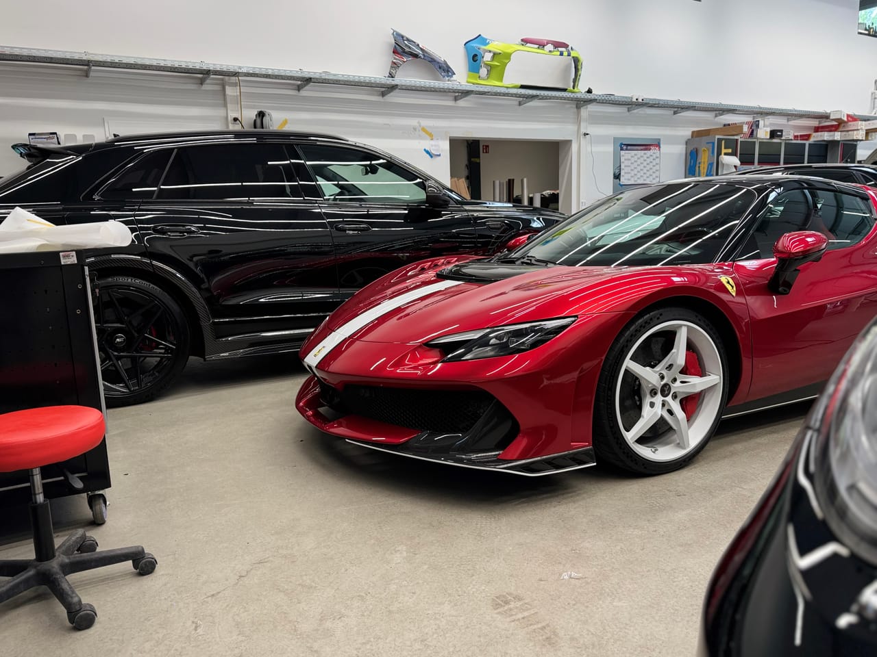 Weite Aufnahme von rotem Ferrari und schwarzem Audi in der Aufbereitungshalle, mehrere Premiumfahrzeuge zugleich.