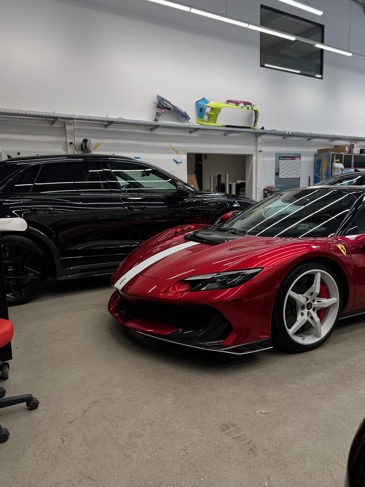 Frontansicht eines roten Ferrari in der Halle, im Hintergrund ein schwarzer Audi RSQ8.