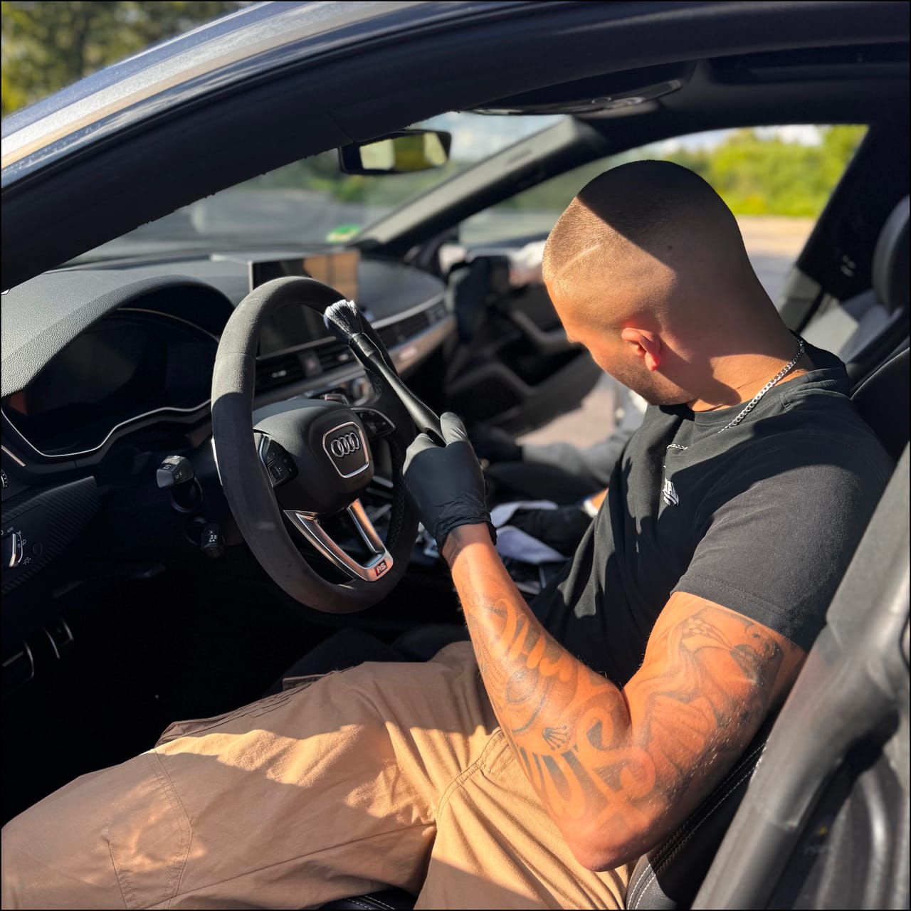 Inhaber Jonas Braun bei der Innenraumaufbereitung am Lenkrad seines Audi RS, sonniger Tag.