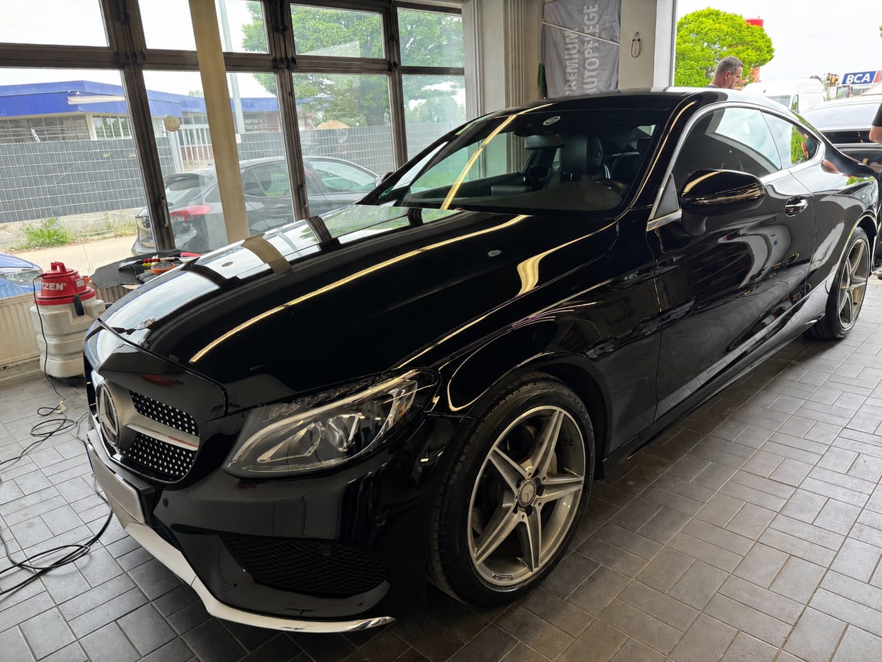 Schwarzes Mercedes C-Coupé von schräg vorne in der Halle, makelloser Hochglanzlack mit deutlichen Lichtstreifen.