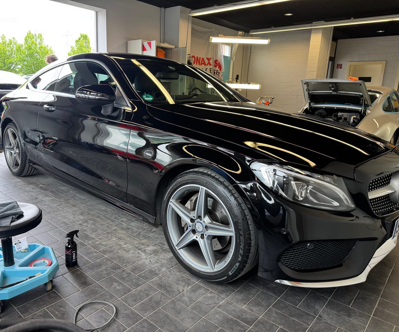 Schwarzes Mercedes C-Klasse Coupé in AMG-Line von schräg vorne in der Aufbereitungshalle, Hochglanzlack mit klaren Reflexen.