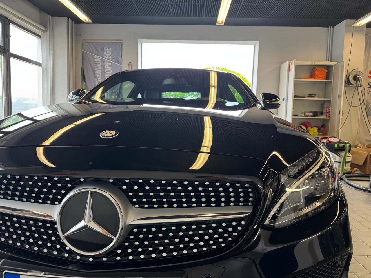 Frontale Nahaufnahme eines schwarzen Mercedes C-Coupé mit Diamantgrill und Stern, klare Lichtreflexe auf der Motorhaube.