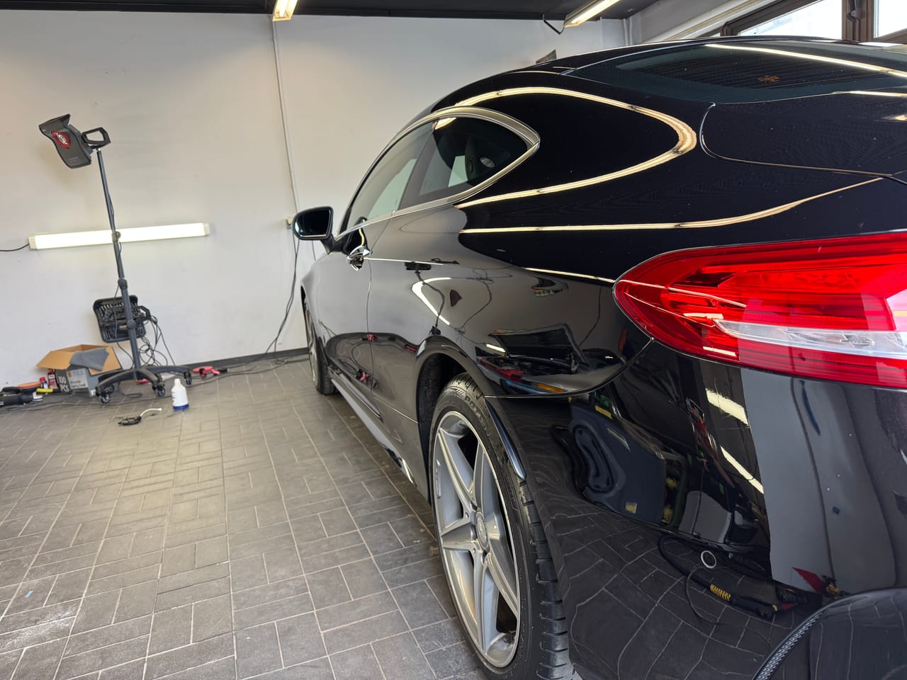 Heckpartie eines schwarzen Mercedes C-Coupé in der Halle, leuchtendes Rücklicht und tiefer, spiegelnder Lack.
