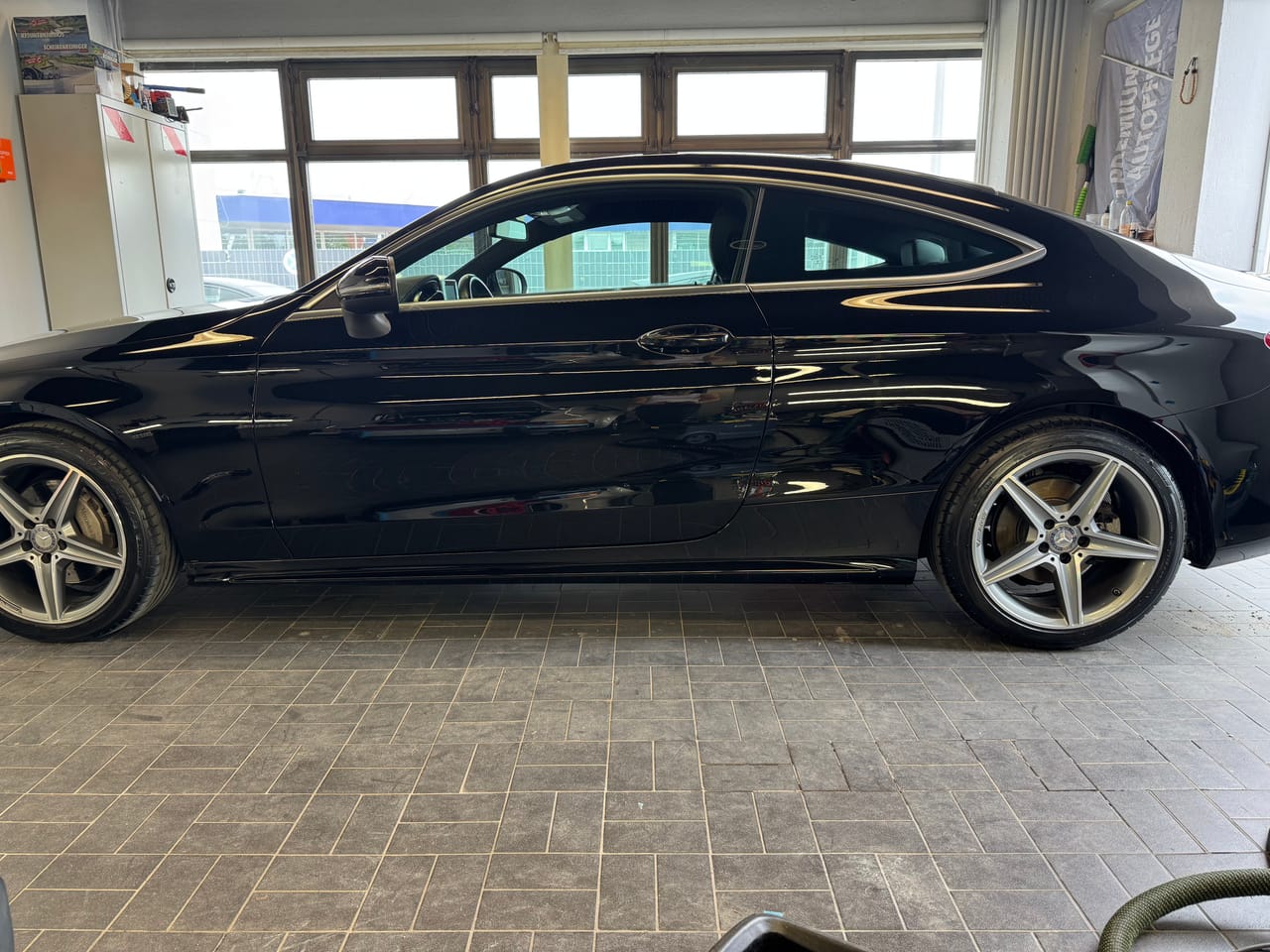 Seitenansicht eines schwarzen Mercedes C-Coupé in der Aufbereitungshalle, glänzende AMG-Felgen und makelloser Lack.